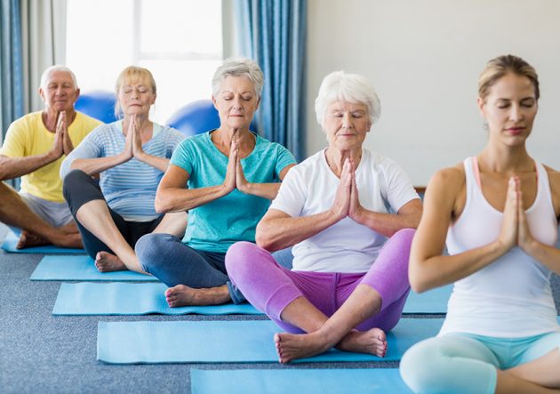 Instructor performing yoga with seniors during sports class